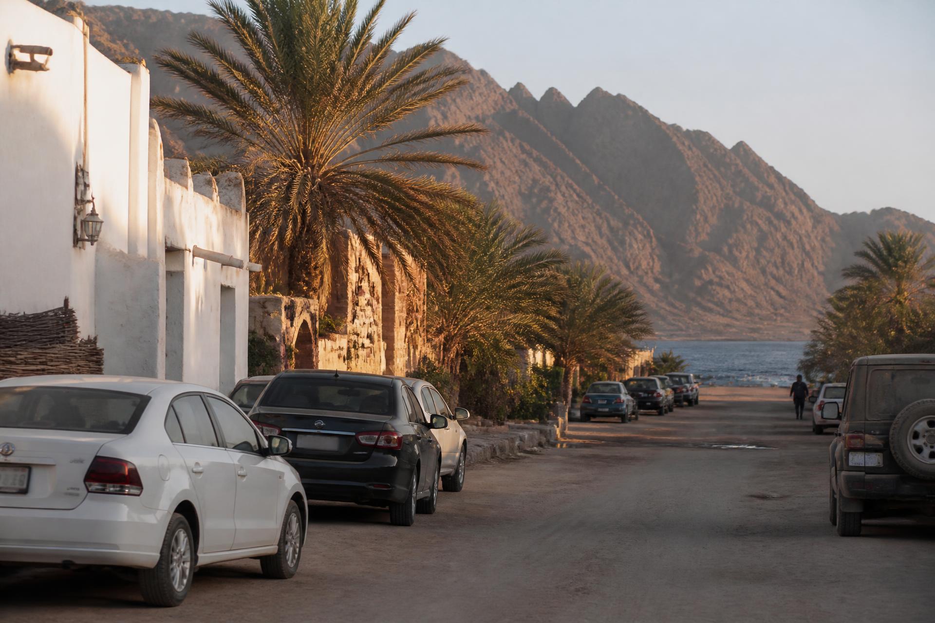 Street in Dahab, South Sinai, with parked cars, palm trees and the Sinai mountains